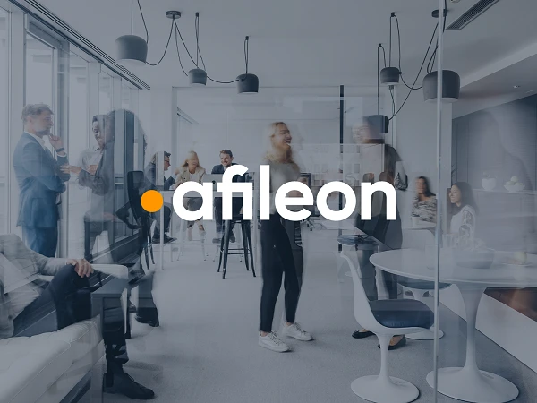 Ein modernes Büro mit mehreren Menschen, die in Gruppen miteinander sprechen oder arbeiten. Im Vordergrund sind eine Gruppe von Personen in lebhaften Gesprächen zu sehen, während im Hintergrund andere Personen am Tisch sitzen oder stehen. Das Logo "afileon" ist prominent in der Mitte des Bildes platziert.