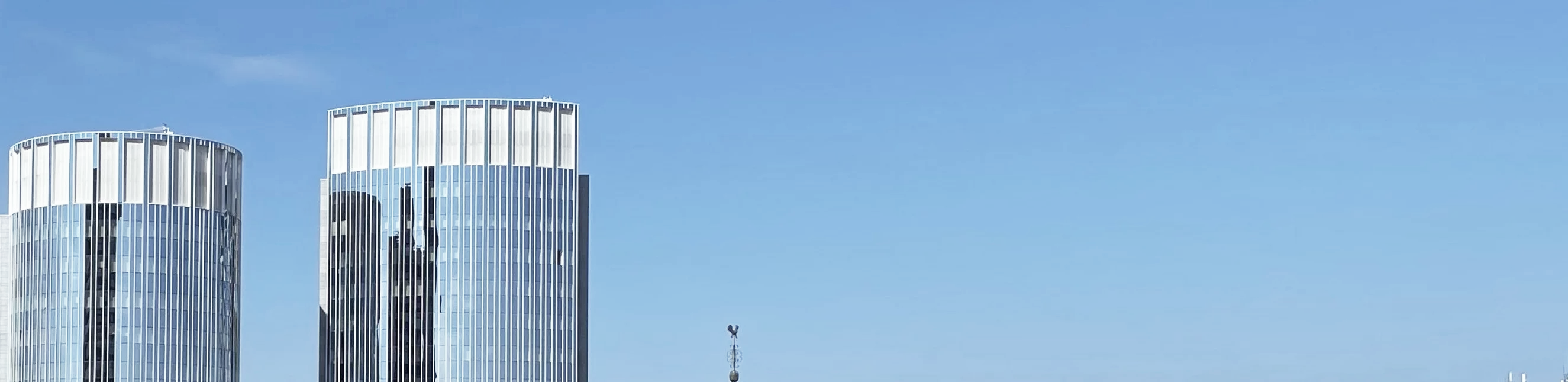 Zwei moderne Hochhäuser mit gläserner Fassade heben sich gegen einen klaren blauen Himmel ab.